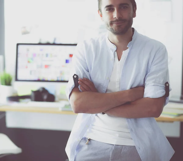 Retrato del joven diseñador delante de la computadora portátil y el ordenador mientras trabaja. Asistente usando su móvil en segundo plano . — Foto de Stock