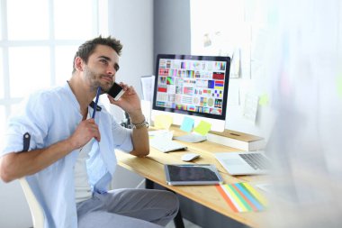 İnternette çalışırken bilgisayarın ve dizüstü bilgisayarın önünde grafik stüdyosunda oturan genç tasarımcının portresi.