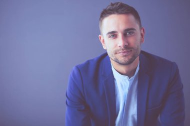 Gri arka planda yalnız oturan genç iş adamı.