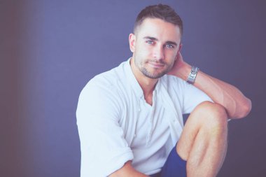 Gri arka planda yalnız oturan genç iş adamı.