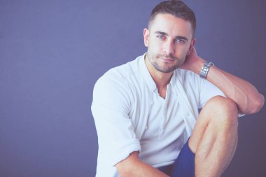 Gri arka planda yalnız oturan genç iş adamı.