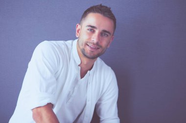 Gri arka planda yalnız oturan genç iş adamı.