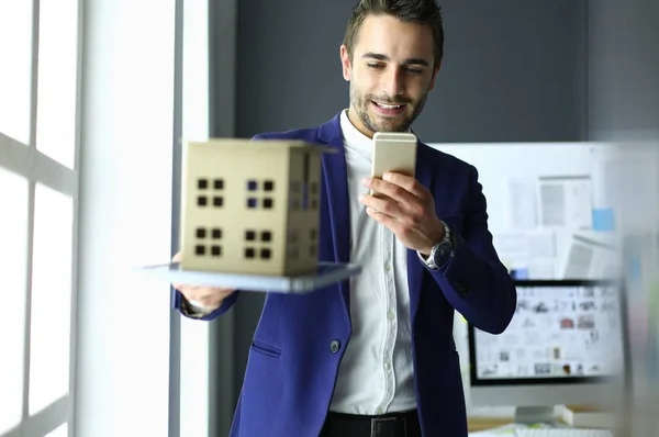 Homme d'affaires tenant maison miniature à portée de main debout dans le bureau . — Photo