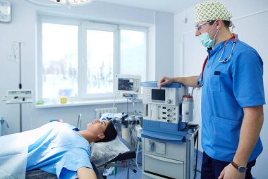 Ameliyat odasında arka planda erkek cerrah var.