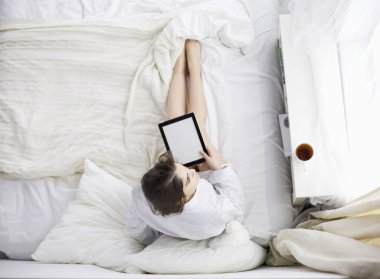Sabahları yatakta otururken tablet kullanan ve kahve içen kadın portresi