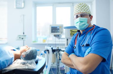 Ameliyat odasında arka planda erkek cerrah var.