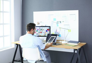 İnternette çalışırken bilgisayarın ve dizüstü bilgisayarın önünde grafik stüdyosunda oturan genç tasarımcının portresi.