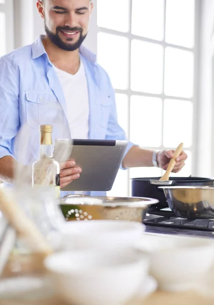 Hombre siguiendo la receta en la tableta digital y cocinar comida sabrosa y saludable en la cocina en casa — Foto de Stock