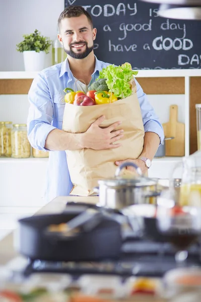 Man met papieren zak vol boodschappen op de keukenachtergrond. Winkelen en gezond voedsel concept — Stockfoto