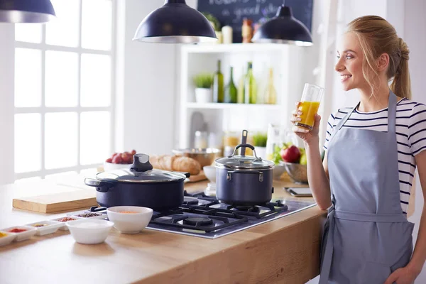 Привлекательная женщина держит стакан апельсинового сока, стоя на кухне — стоковое фото