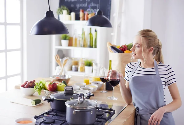 Mujer bonita bebiendo un poco de vino en casa en la cocina —  Fotos de Stock