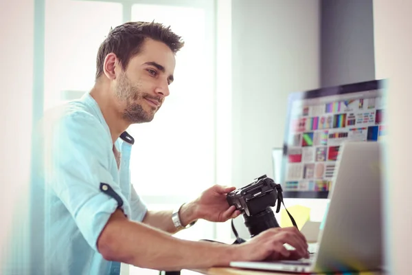 Portret van jonge ontwerper zittend in grafische studio achter laptop en computer terwijl hij online werkt. — Stockfoto