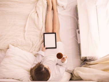 Sabahları yatakta otururken tablet kullanan ve kahve içen kadın portresi