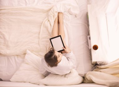 Sabahları yatakta otururken tablet kullanan ve kahve içen kadın portresi