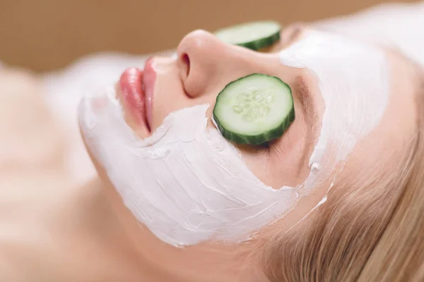 Belle jeune femme recevant un masque facial de concombre dans un salon de beauté — Photo