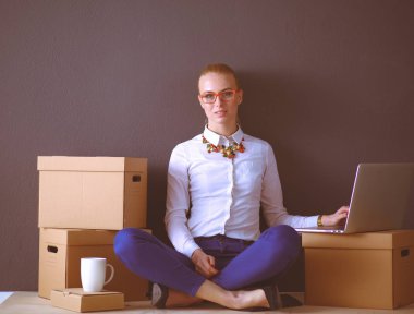 Kadın yerde dizüstü bilgisayarlı bir kutunun yanında oturuyor.