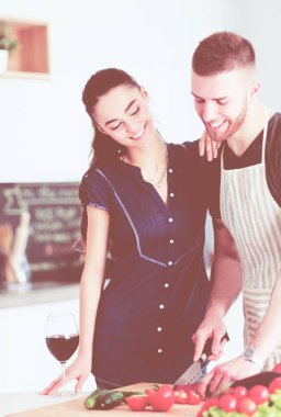 Sebze doğrayan genç bir adam ve mutfakta dizüstü bilgisayarı olan bir kadın.