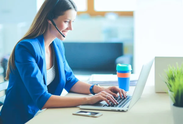 Portrait of beautiful business woman working at her desk with headset and laptop.. — Stock Photo, Image
