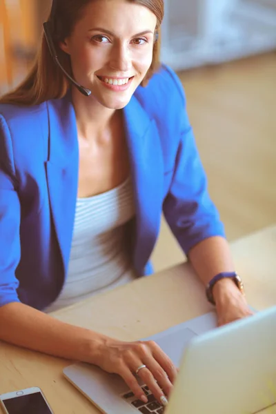 Retrato de mulher de negócios bonita trabalhando em sua mesa com fone de ouvido e laptop. — Fotografia de Stock