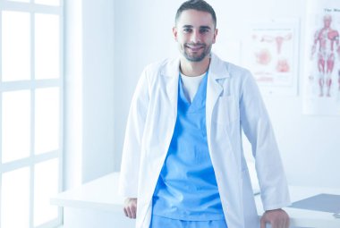 Genç ve kendinden emin erkek doktor portresi tıp ofisinde duruyor.