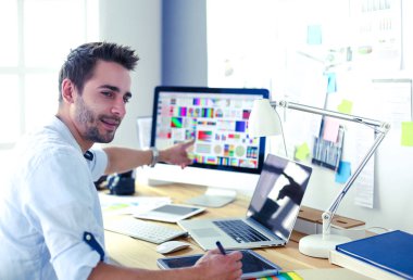 İnternette çalışırken bilgisayarın ve dizüstü bilgisayarın önünde grafik stüdyosunda oturan genç tasarımcının portresi.