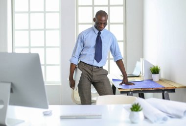 Ofiste bilgisayar ve planlarla çalışan Afrikalı Amerikalı bir mimar.