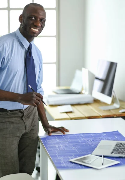 Africký americký architekt pracující s počítačem a plány v kanceláři — Stock fotografie