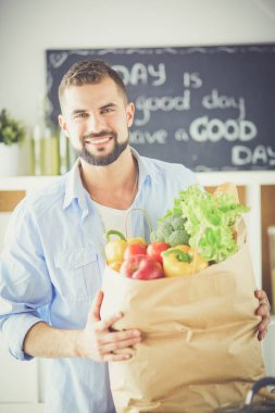 Mutfak arka planında poşet dolusu erzak tutan adam. Alışveriş ve sağlıklı gıda konsepti
