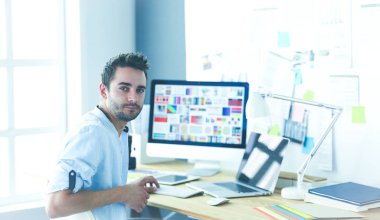 İnternette çalışırken bilgisayarın ve dizüstü bilgisayarın önünde grafik stüdyosunda oturan genç tasarımcının portresi.