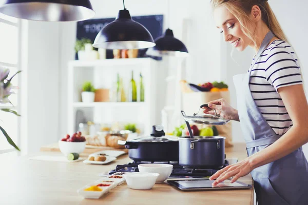 Jovem usando um computador tablet para cozinhar em sua cozinha — Fotografia de Stock