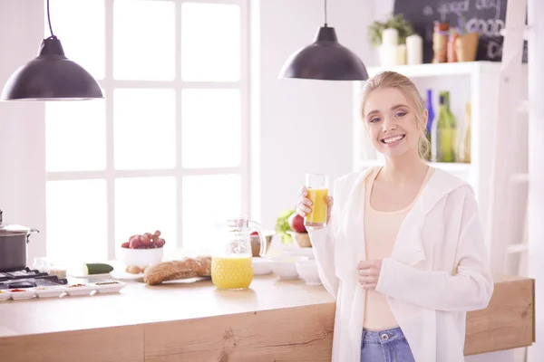 Mulher atraente segurando um copo de suco de laranja enquanto estava na cozinha — Fotografia de Stock