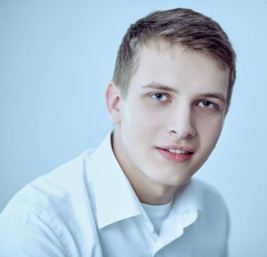 Gri arka plan üzerinde oturan gülümseyen genç adam portresi. Genç adam portresi