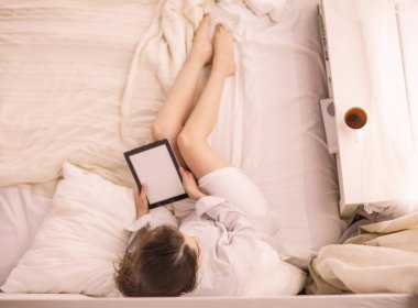 Sabahları yatakta otururken tablet kullanan ve kahve içen kadın portresi
