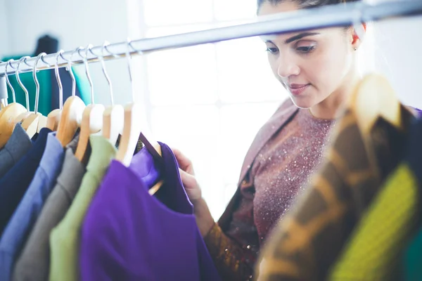 Beautiful young stylist near rack with hangers — Stock Photo, Image