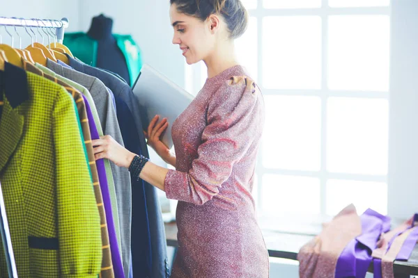 Vacker ung stylist nära rack med hängare — Stockfoto