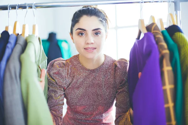 Schöne junge Stylistin in der Nähe von Gestell mit Kleiderbügeln — Stockfoto