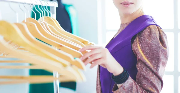 Schöne junge Stylistin in der Nähe von Gestell mit Kleiderbügeln — Stockfoto