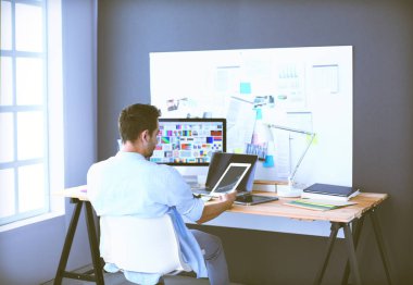 İnternette çalışırken bilgisayarın ve dizüstü bilgisayarın önünde grafik stüdyosunda oturan genç tasarımcının portresi.