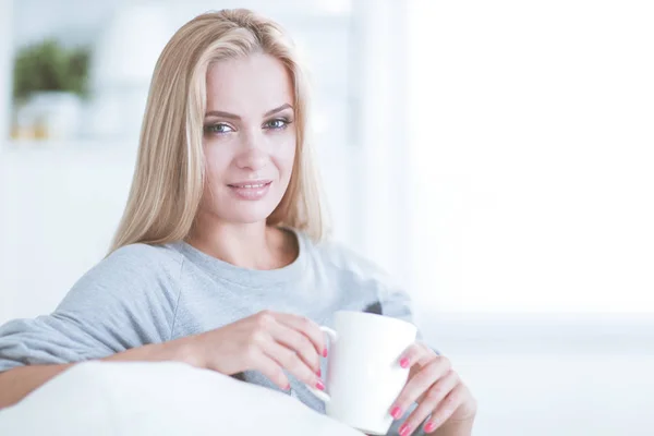 Портрет молодой женщины, сидящей на диване с чашкой кофе — стоковое фото