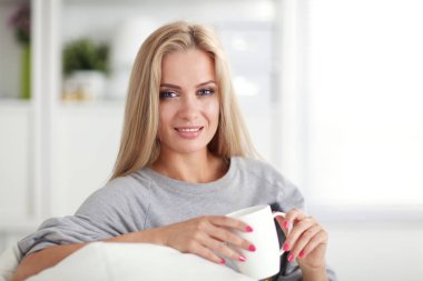 Ellerini içine ile kanepede oturan ve onun önünde göründüğü gülümseyen kadın