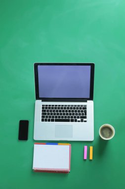 Dizüstü bilgisayar, akıllı telefon, kahve ve malzemeleri fincan, yeşil arka plan üzerinde izole ofis masası, düz yatıyordu