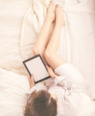 Sabahları yatakta otururken tablet kullanan ve kahve içen kadın portresi