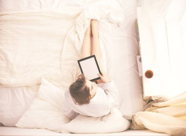 Sabahları yatakta otururken tablet kullanan ve kahve içen kadın portresi