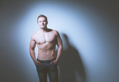Gri arka plan üzerinde duran bir yakışıklı kaslı adam portresi