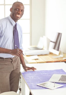 Ofiste bilgisayar ve planlarla çalışan Afrikalı Amerikalı bir mimar.