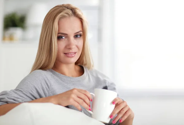 Portrett av en ung kvinne som sitter på sofaen med en kopp kaffe – stockfoto