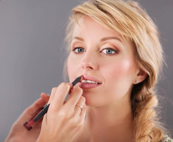 Vacker kvinna ansikte. Hand make-up Master, målning läppar av ung skönhet modell flicka — Stockfoto