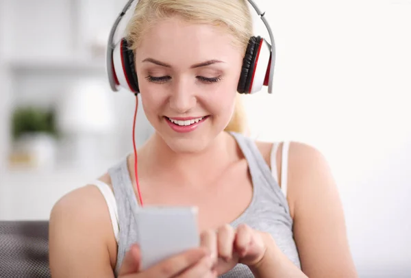 Mujer sonriente escuchando música en auriculares y usando un teléfono inteligente —  Fotos de Stock