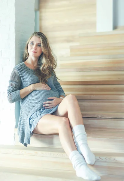 Krásná mladá těhotná žena sedí na schodech dřevěné schodiště — Stock fotografie