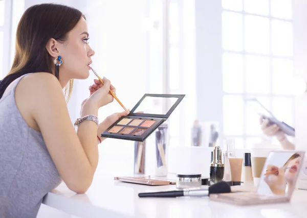 Mujer morena aplicando maquillaje para una cita nocturna frente a un espejo —  Fotos de Stock